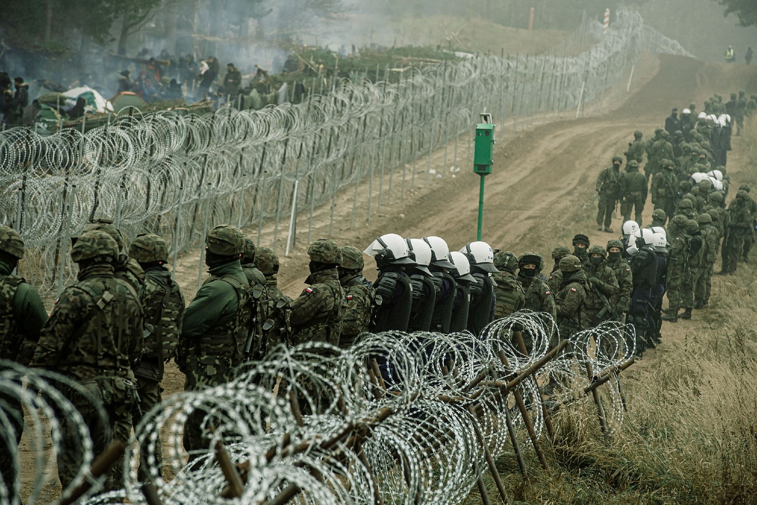 Polish soldiers and police watch migrants at the Poland/Belarus border near Kuznica, Poland, in this photograph released by the Territorial Defence Forces, November 12, 2021. Irek Dorozanski/DWOT/Handout via Reuters