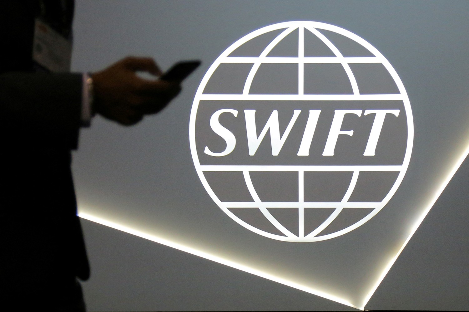  FILE PHOTO: A man using a mobile phone passes the logo of global secure financial messaging services cooperative SWIFT at the SIBOS banking and financial conference in Toronto, Ontario, Canada October 19, 2017. Reuters/Chris Helgren/File Photo